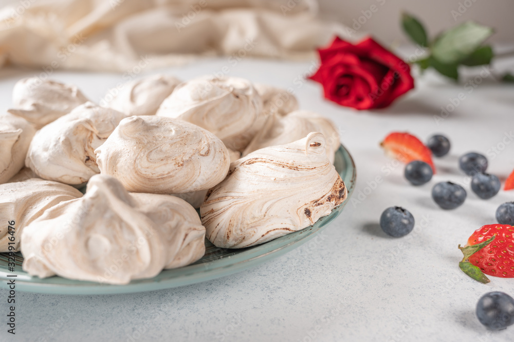 Homemade dessert meringue on a plate on white background. Napkin, strawberry and blueberry berries and red rose flower Homemade dessert meringue on a plate on white background. Napkin, strawberry and blueberry berries and red rose flower
