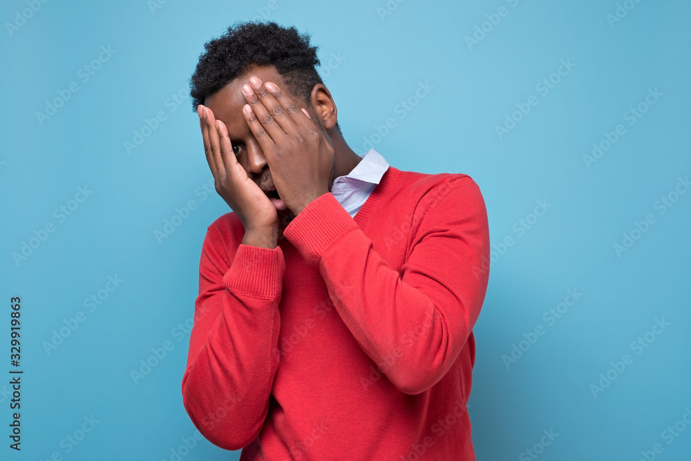 The african american man is very upset, he covered his face with his hands on blue background