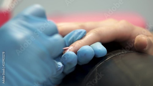 Manicure master applies pink varnish on the client’s nails with a brush.