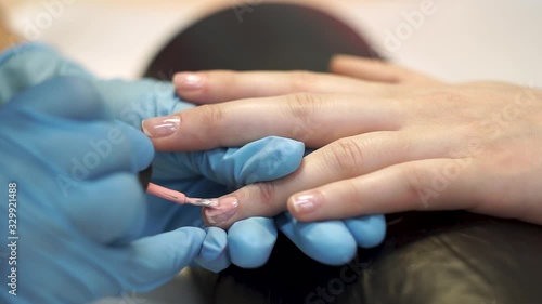 Manicure master applies pink varnish on the client’s nails with a brush.