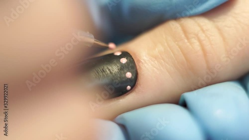Manicurist draws pink dots on the client’s black nail
