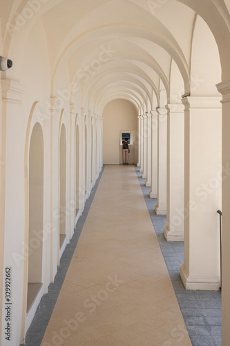 Woman looks out of a small window at the end of a colonnade