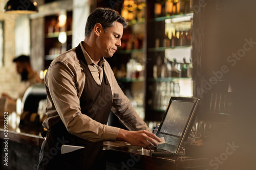 Male waiter going through orders while working at cash register in a bar.