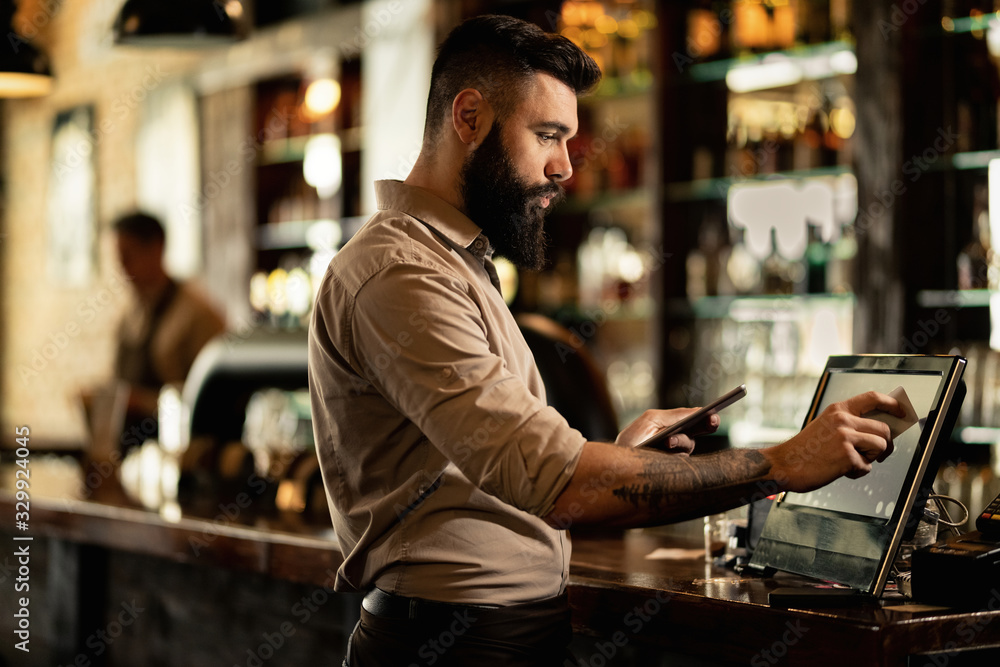 Young bartender using cash register while working in a pub. - obrazy, fototapety, plakaty 