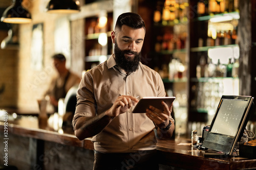 Smiling barista using digital tablet while working in a bar.