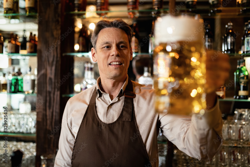 Happy mid adult barista with glass of beer in a pub. Happy mid adult barista with glass of beer in a pub.