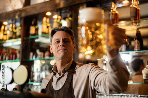 Smiling bartender holding glass of craft beer in a pub.