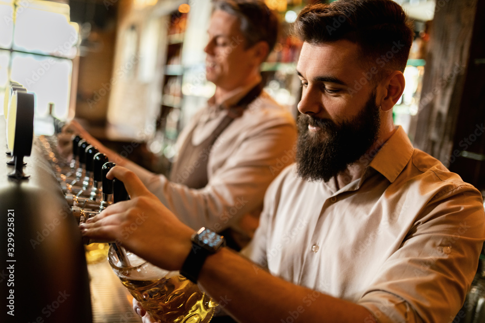 Bartenders pouring beer from beer tap while working in a bar.