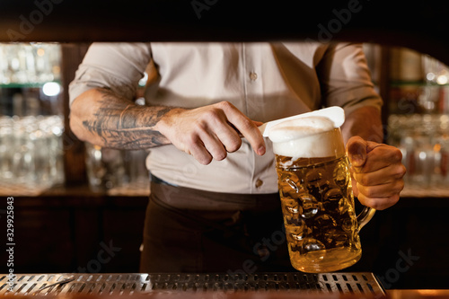 Unrecognizable barista removing beer froth while serving beer in a bar.