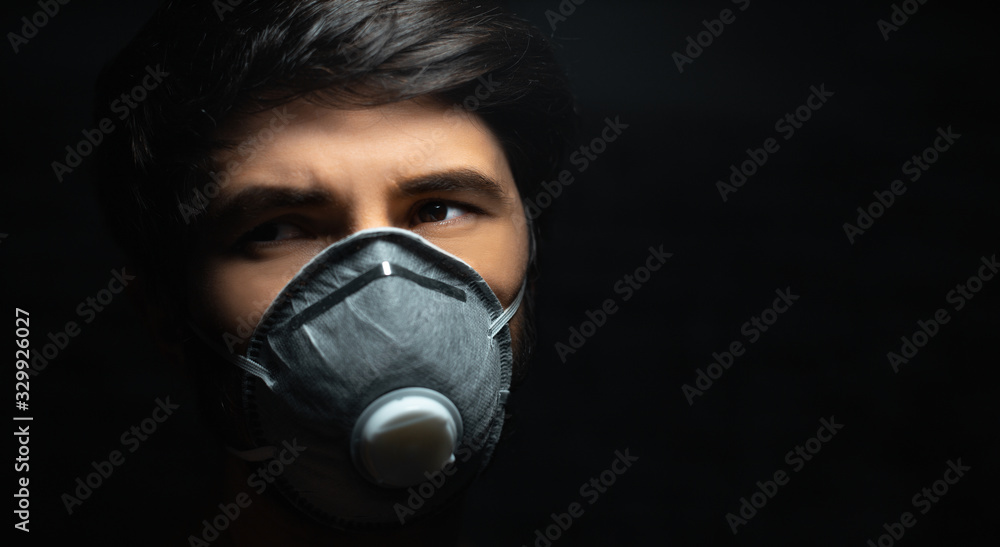 Dramatic dark portrait of ill young man with protective mask on black background with copy space.