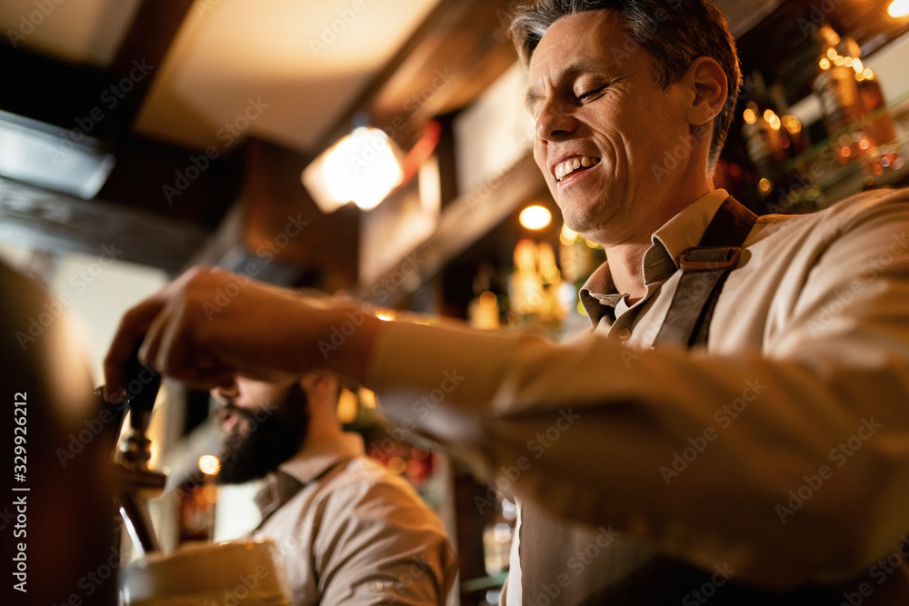 Below view of happy bartender pouring beer form beer tap in a bar.