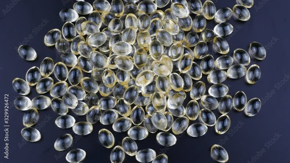 Golden capsules of vitamin D on a black background slowly rotate clockwise. Golden capsules of vitamin D on a black background slowly rotate clockwise.