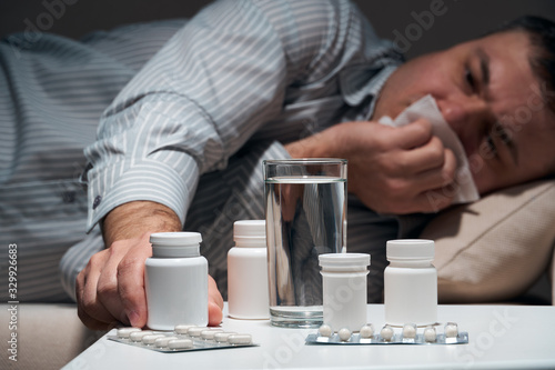 Overworked businessman is lying on the sofa and resting. Pills and glass of water near him.