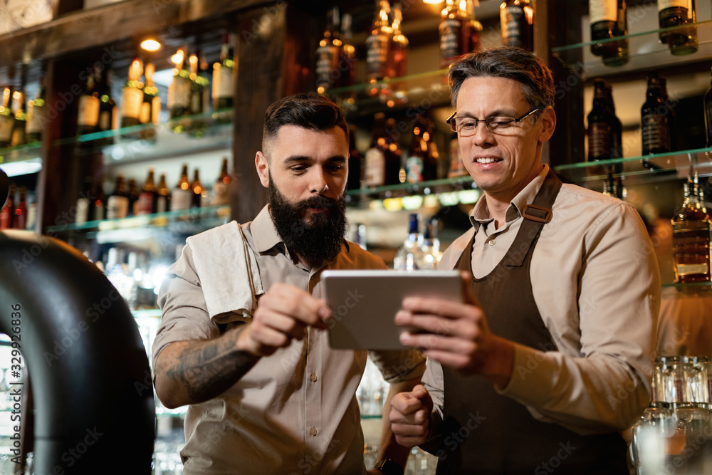 Two bartenders using digital tablet while working in a bar. Two bartenders using digital tablet while working in a bar.