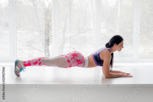 Athletic young girl performs exercises in the Studio on a light background. Fitness, healthy lifestyle