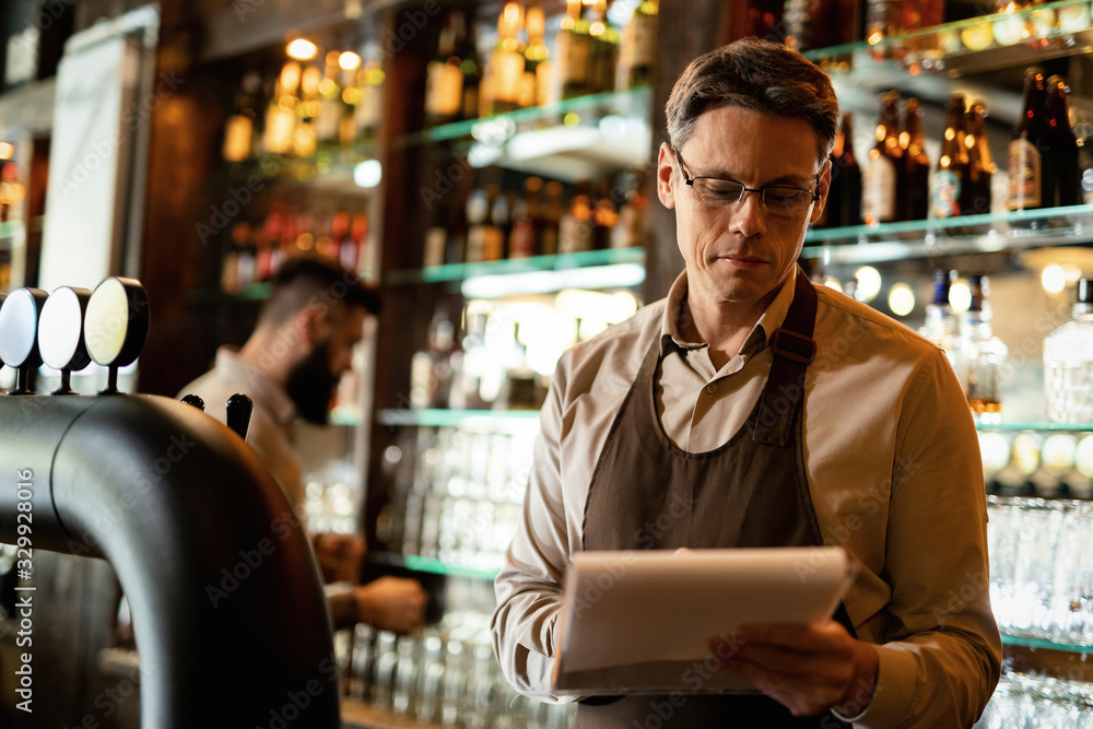 Mid adult barista going through inventory list at bar counter. Mid adult barista going through inventory list at bar counter.