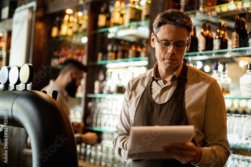 Mid adult barista going through inventory list at bar counter.