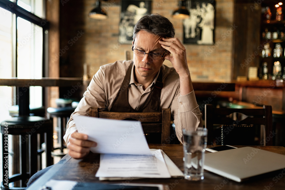 Mid adult waiter going through inventory list while sitting in a pub. Mid adult waiter going through inventory list while sitting in a pub.