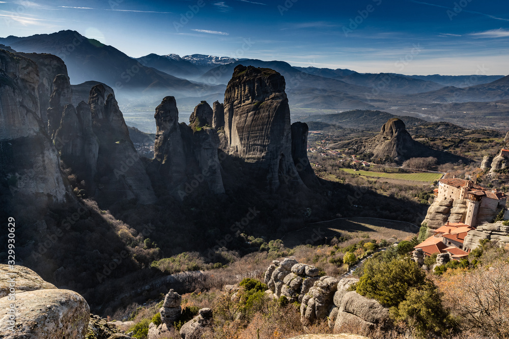 Aerial view of monastery Rousanou and breathtaking picturesque valley and landmark canyon of Meteora at sunset, Kalambaka, Greece, shadows, twisted road, bridge