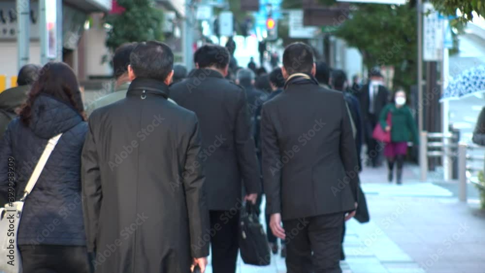 TOKYO, JAPAN - MARCH 2020 : View of crowd of people walking down the street in busy morning rush hour. Many commuters going to work. Japanese business, job and lifestyle concept. Slow motion shot.
