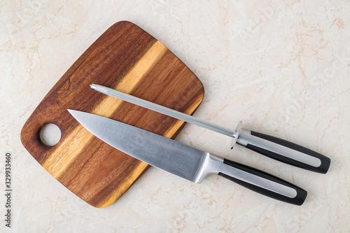 Professional chef knife and a sharpening steel on a wooden cutting board over a kitchen table. Modern kitchen utensils made of high carbon molybdenum vanadium steel. photo