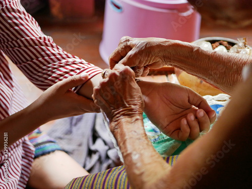 Hand of old woman waving a white string ( Sai Sin ) around her granddaughter hands - Thai traditional blessing from an elder one