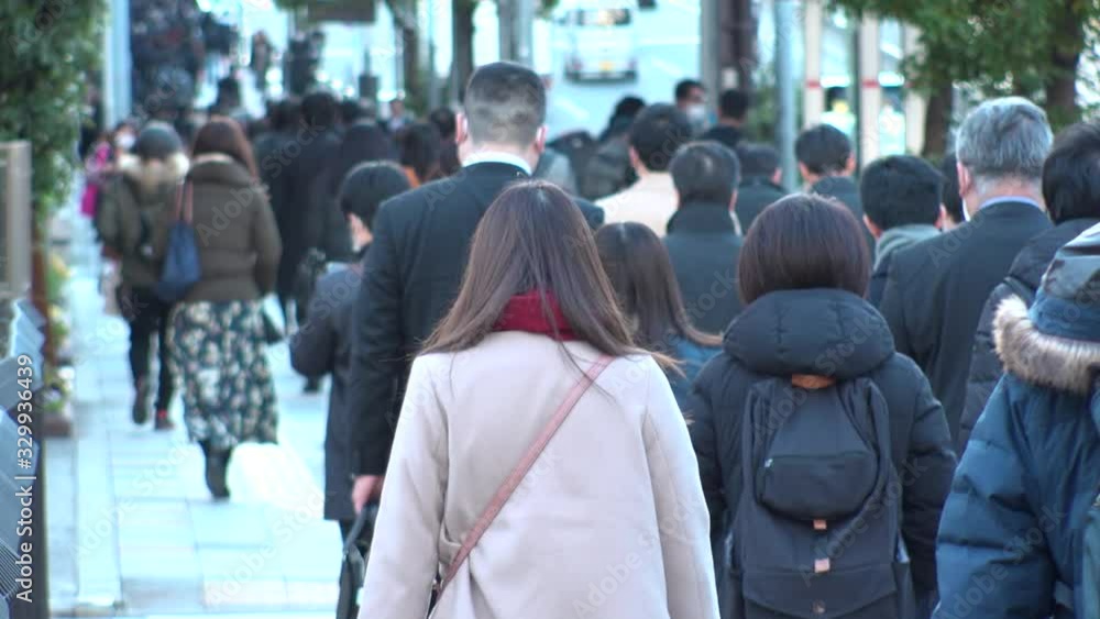 TOKYO, JAPAN - MARCH 2020 : View of crowd of people walking down the street in busy morning rush hour. Many commuters going to work. Japanese business, job and lifestyle concept. Slow motion shot. TOKYO, JAPAN - MARCH 2020 : View of crowd of people walking down the street in busy morning rush hour. Many commuters going to work. Japanese business, job and lifestyle concept. Slow motion shot.