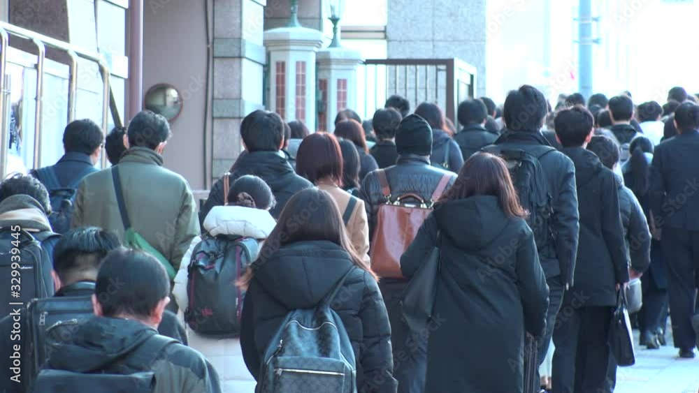 TOKYO, JAPAN - MARCH 2020 : View of crowd of people walking down the street in busy morning rush hour. Many commuters going to work. Japanese business, job and lifestyle concept. Slow motion shot. TOKYO, JAPAN - MARCH 2020 : View of crowd of people walking down the street in busy morning rush hour. Many commuters going to work. Japanese business, job and lifestyle concept. Slow motion shot.