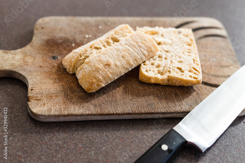 ciabatta bread cut in half on cutting board with knife next to it