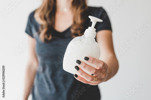 washing your hands concept, woman holding bottle of liquid soap towards the camera