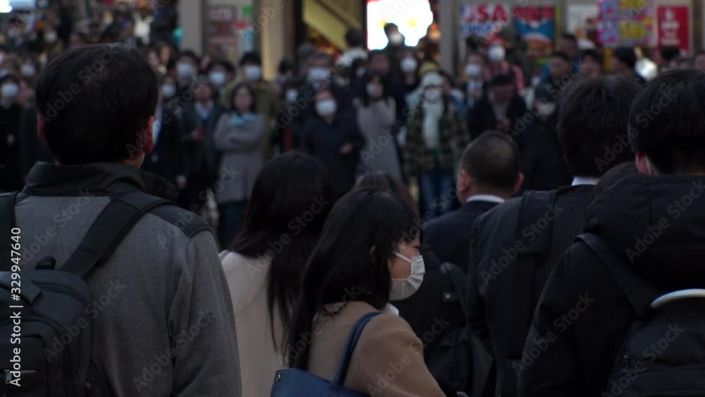 TOKYO, JAPAN - MARCH 2020 : Crowd of people at the street near Shinjuku station in rush hour. Commuters and tourists wearing surgical mask to protect from Coronavirus(COVID-19) or cold. Slow motion. TOKYO, JAPAN - MARCH 2020 : Crowd of people at the street near Shinjuku station in rush hour. Commuters and tourists wearing surgical mask to protect from Coronavirus(COVID-19) or cold. Slow motion.