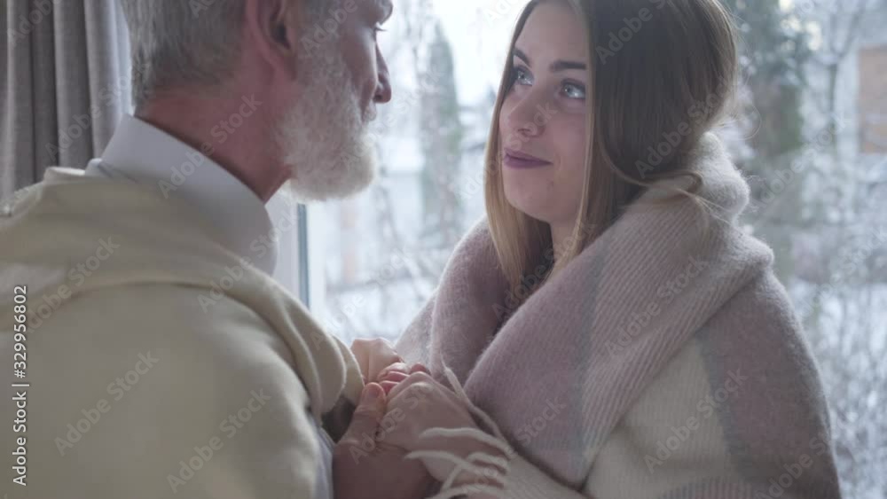 Close-up of cute Caucasian young woman looking at senior man and listening to him with interest. Loving girl spending day with middle-aged partner indoors. Love, lifestyle, affection, leisure. Close-up of cute Caucasian young woman looking at senior man and listening to him with interest. Loving girl spending day with middle-aged partner indoors. Love, lifestyle, affection, leisure.