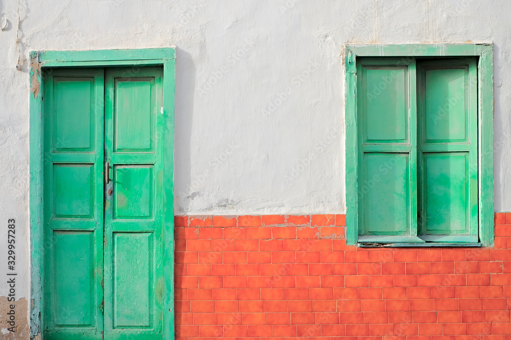 A green door and a green window in a wall with red bricks.