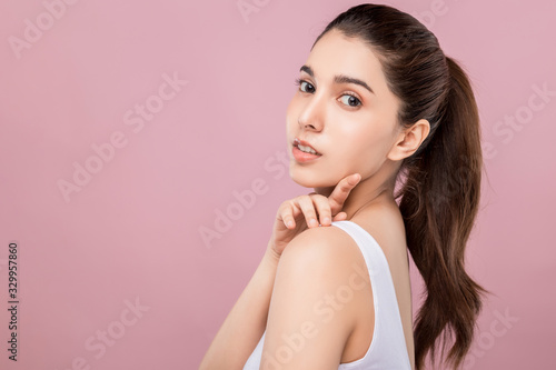 Young attractive Caucasian woman with smiley face and healthy skin touching her shoulder isolated on pink.