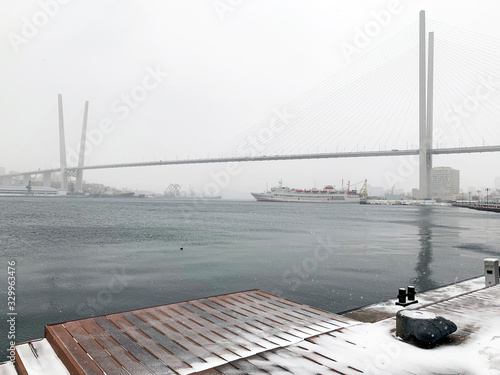 Russia, Vladivostok. Golden bridge- cable- stayed bridge over the Golden horn Bay during a heavy snowfall during the  cyclone from the side of Tsesarevich embankment photo