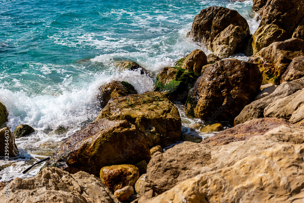 A close-up shot of the Mediterranean Sea turquoise water and powerful waves beating against the rocks on the coast