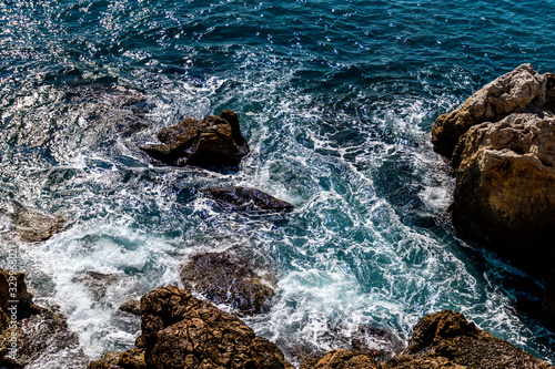 A close-up shot of the Mediterranean Sea turquoise water and powerful waves beating against the rocks on the coast