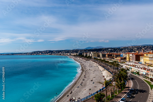 Panoramic wide angle shot of the Quai des États-Unis, people relaxing on the beach of the Mediterranean Sea coastline with the sunlight reflecting in the turquoise water (Nice, France)