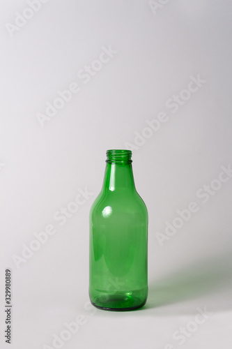 Small empty green glass bottle without cover and label on bright grey background. Can be used as mock up for juice or beer.