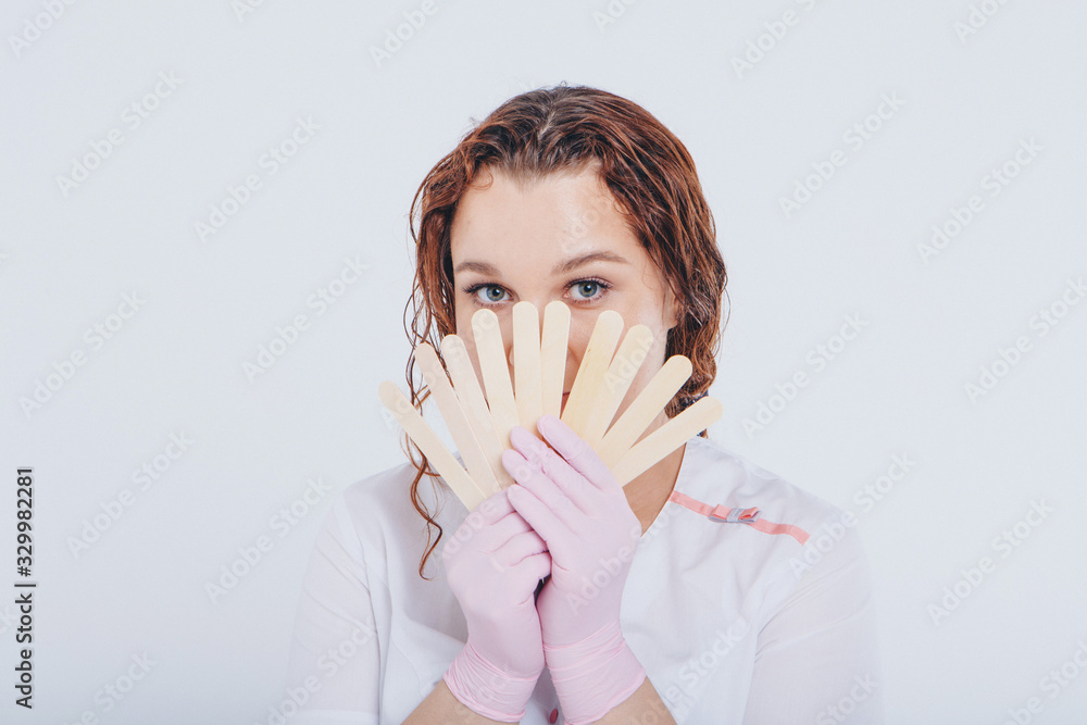 a girl in a white coat with wooden sticks in her hands. the doctor is preparing for waxing. Medicine concept, medical instruments, health care , beauty industry, hair removal, natural material a girl in a white coat with wooden sticks in her hands. the doctor is preparing for waxing. Medicine concept, medical instruments, health care , beauty industry, hair removal, natural material