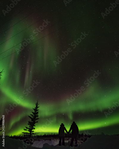 Aurora Borealis Northern Lights Yukon Territory Canada with two people, couple holding hands with magnificent arctic dancing sky behind. Tourism, tourists, vacation, love, romantic, couple. photo