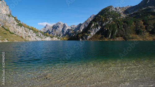 Sunny autumn alpine Tappenkarsee lake and rocky mountains above, Austria. Panoramic camera moving.  Picturesque hiking, seasonal, and nature beauty concept high resolution scene.