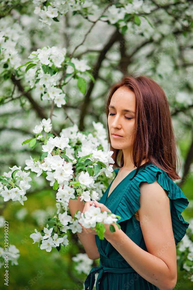 A beautiful young brunette stands near a blooming Apple tree on a warm spring day. Springtime A beautiful young brunette stands near a blooming Apple tree on a warm spring day. Springtime