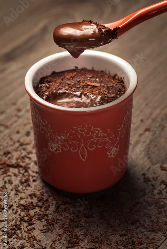 chocolate pudding in a red pot with cream on a spoon and chocolate chips on the grey table