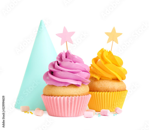 Delicious birthday cupcakes and party cap on white background