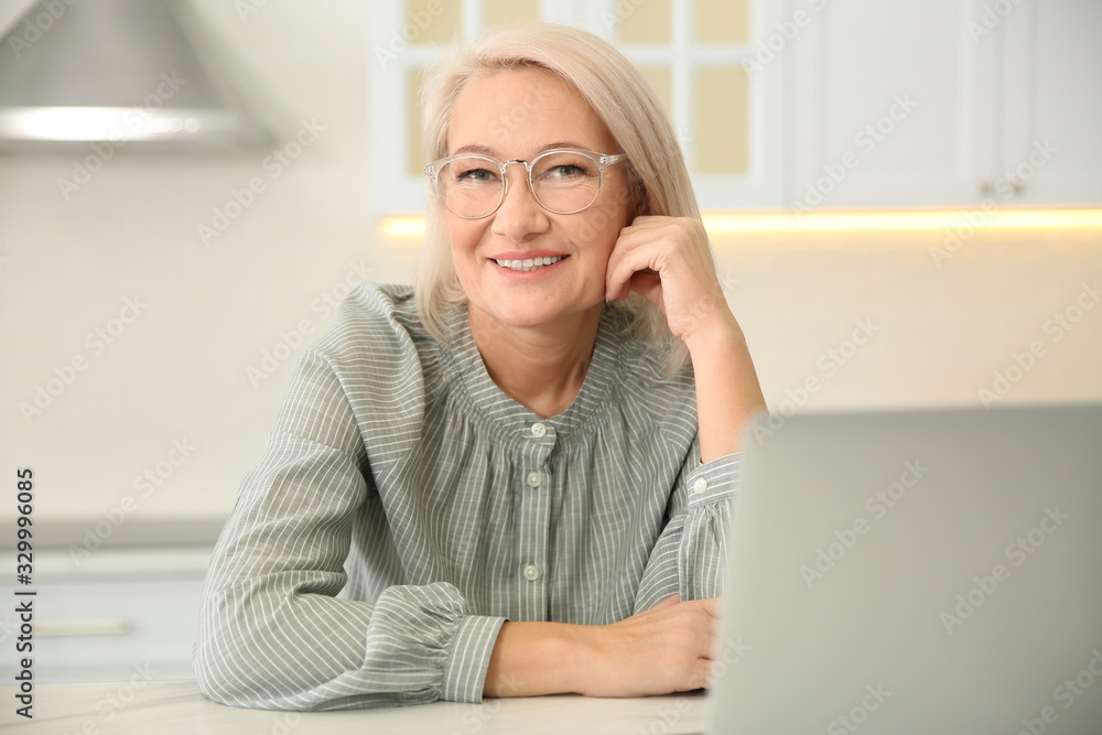 Beautiful mature woman working with laptop in kitchen Beautiful mature woman working with laptop in kitchen