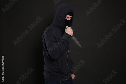 Man in mask with knife on black background. Dangerous criminal