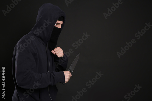 Man in mask with knife on black background, space for text. Dangerous criminal