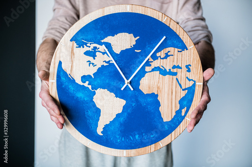 The wooden clock is filled with epoxy resin with a map of the world in the style of the LOFT. Man with clock on white background.