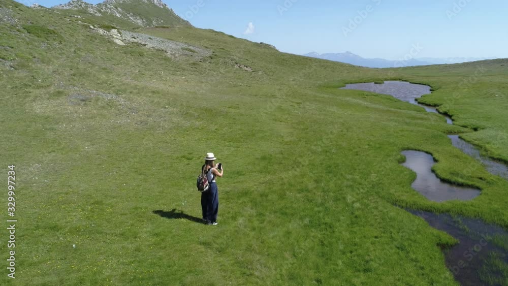High view of woman taking a selfie on her smartphone next to an alpine lake in Grammos mountain, Greece, drone High view of woman taking a selfie on her smartphone next to an alpine lake in Grammos mountain, Greece, drone